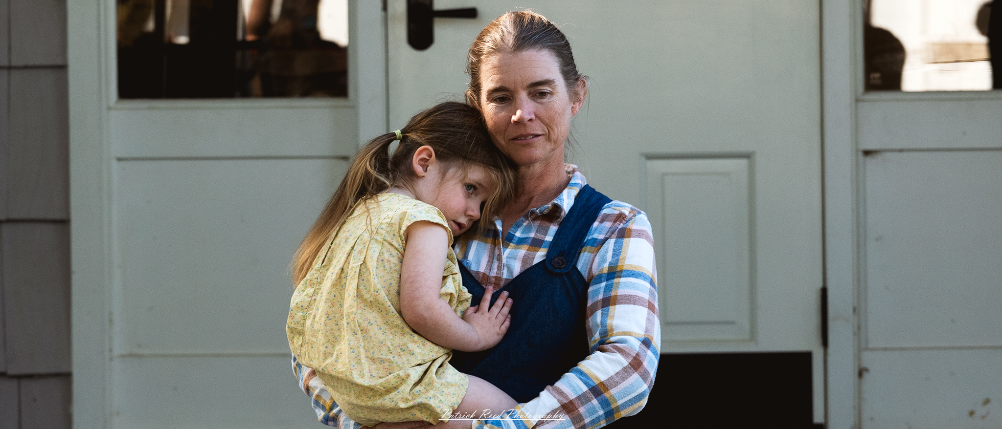 A woman gently cradles a child in her arms, showcasing a tender and nurturing moment. The woman has a warm smile, her hair styled in a simple yet elegant manner, and she wears a soft, flowing dress that highlights her loving demeanor. The child, with bright eyes and a joyful expression, is snuggled close, creating a heartwarming scene of maternal affection. The background may include a serene outdoor setting, such as a park or garden, enhancing the peaceful atmosphere of this intimate moment.